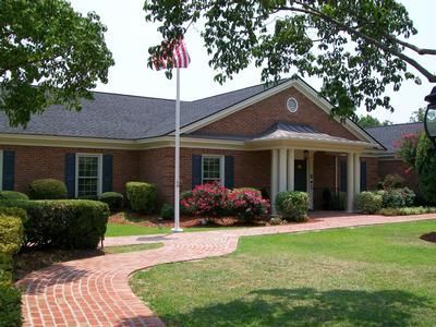 Brick building with white columns, American flag, and curved brick walkway amid green lawn and shrubs
