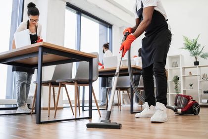 People cleaning an industrial workspace with mops and gloves, one worker smiling at the camera
