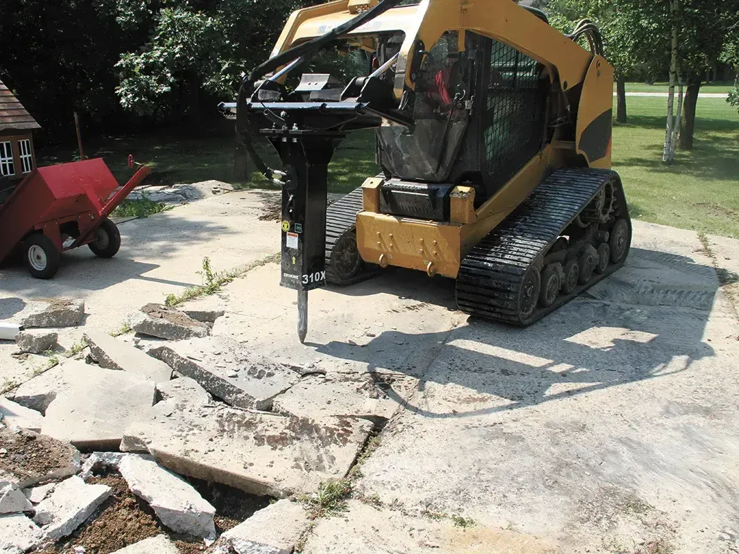 Track loader with a jack hammer attachment demolishing a concrete pad in Conroe, Texas.