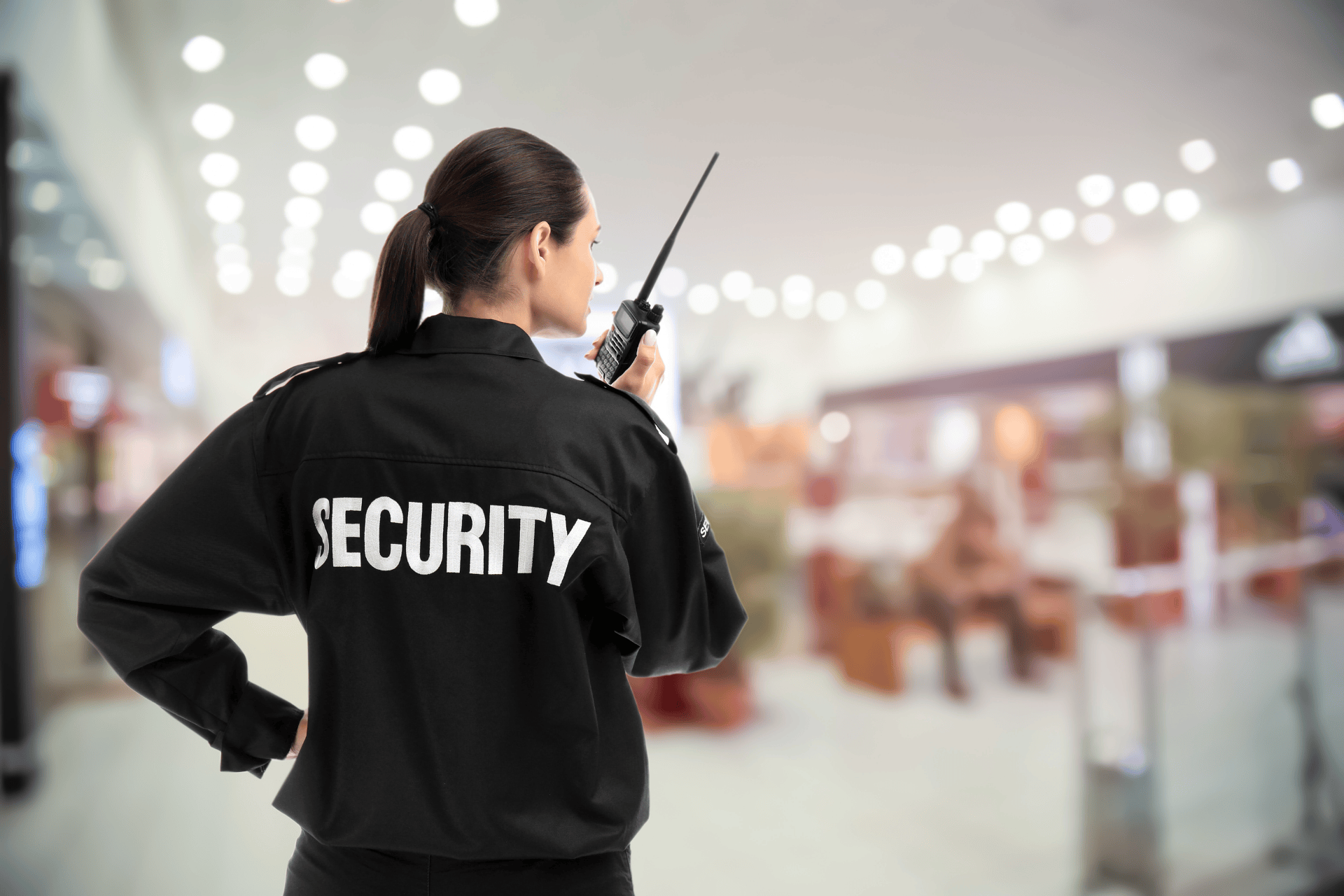 Security guard patrolling a shopping mall while communicating on a walkie-talkie, monitoring activity to prevent retail theft.
