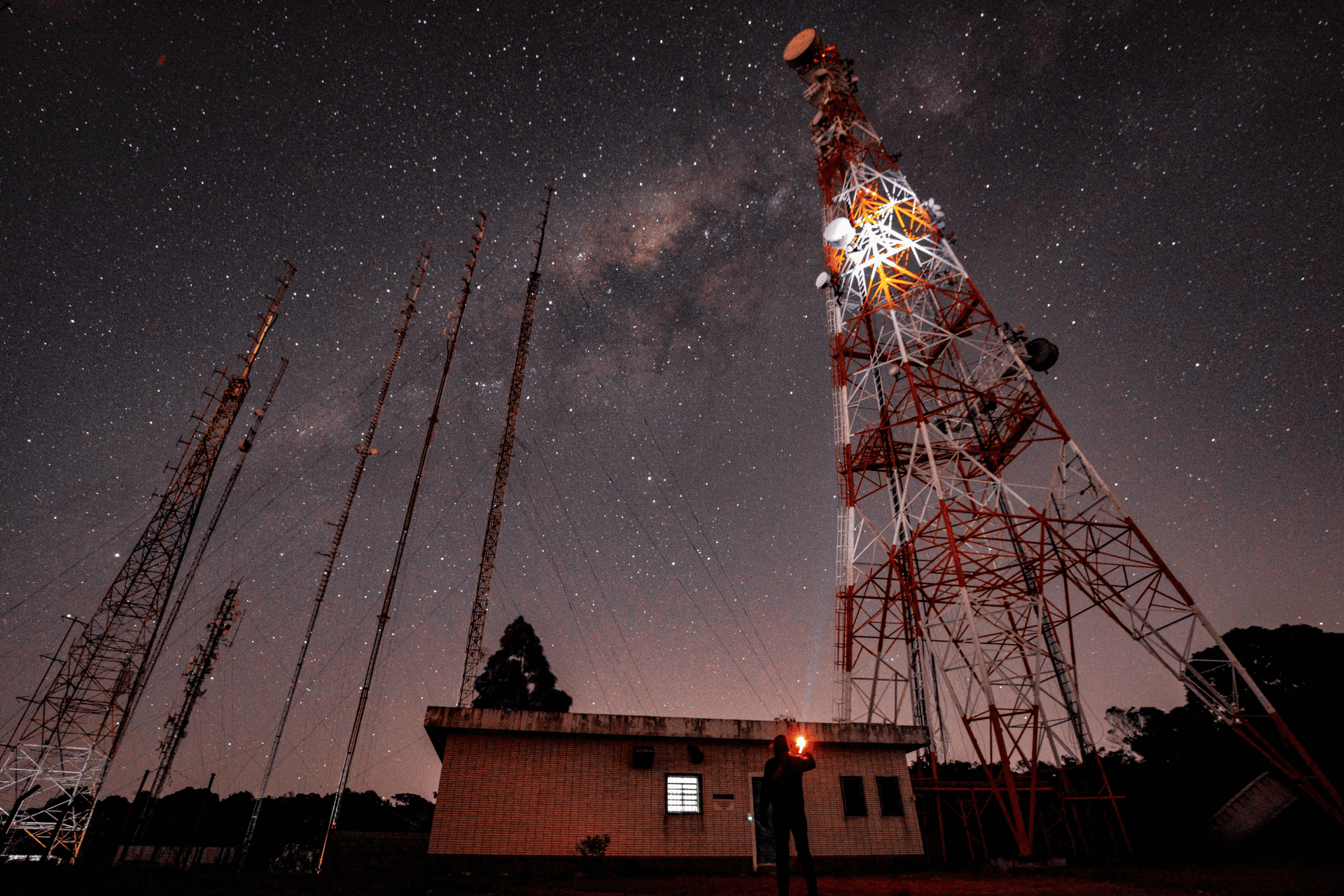 Telecommunications towers and antennas under a starry night sky with the Milky Way visible, and a pe