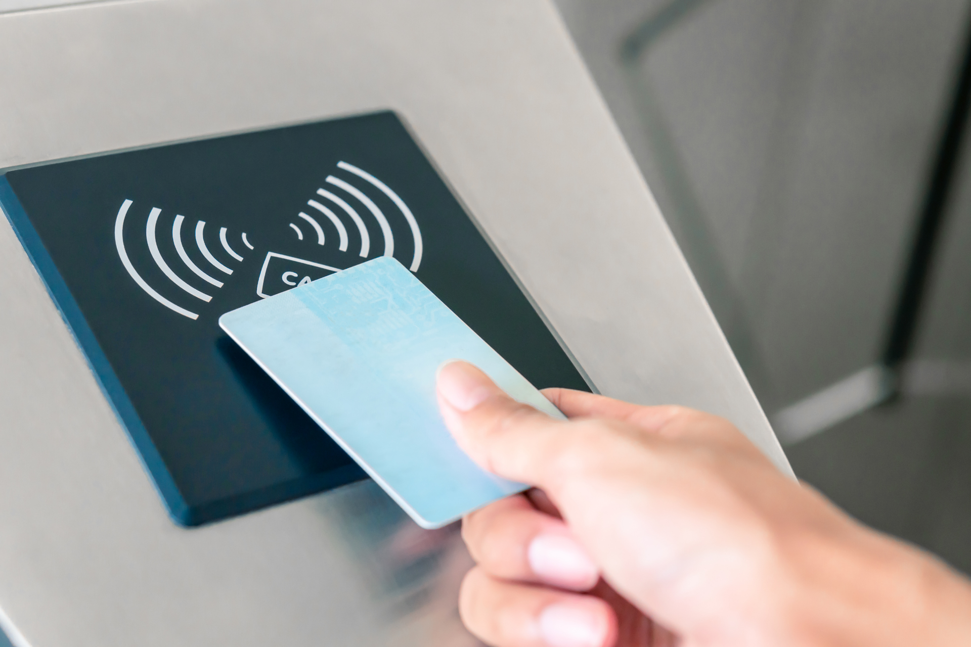 Hand tapping a blue contactless card on an RFID reader panel with a wireless signal icon.