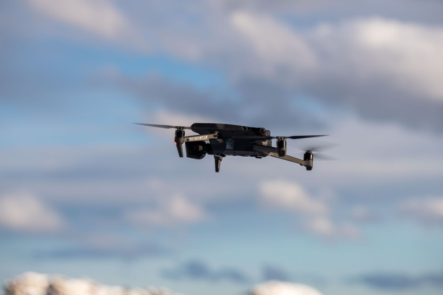 Black drone flying against a cloudy blue sky