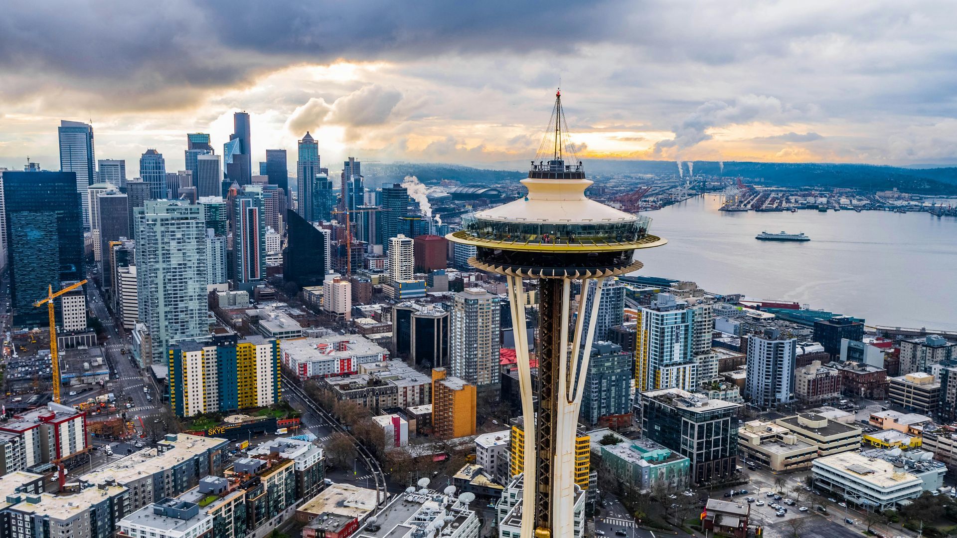 Seattle cityscape with Space Needle in foreground, Puget Sound and skyline in background, cloudy sky.