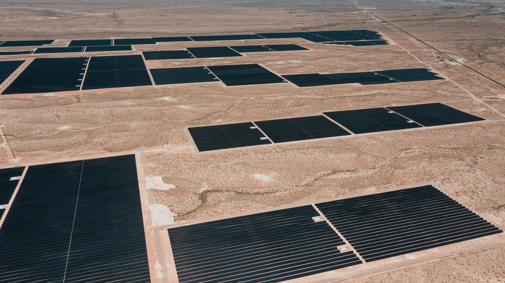 Rows of black solar panels spread across a dry desert landscape.