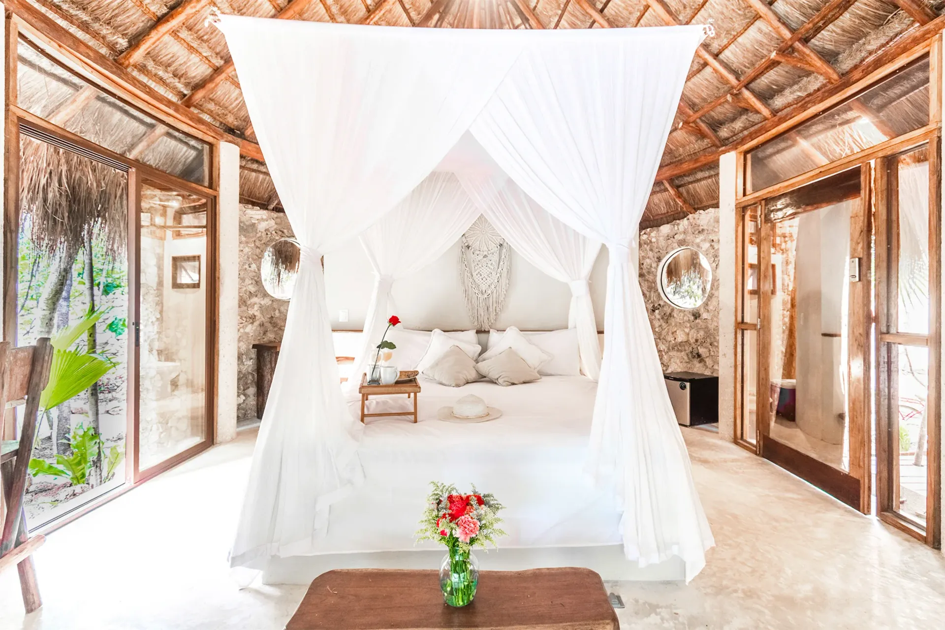 Acogedor dormitorio blanco con una cama con dosel, detalles de madera y un ramo de flores.