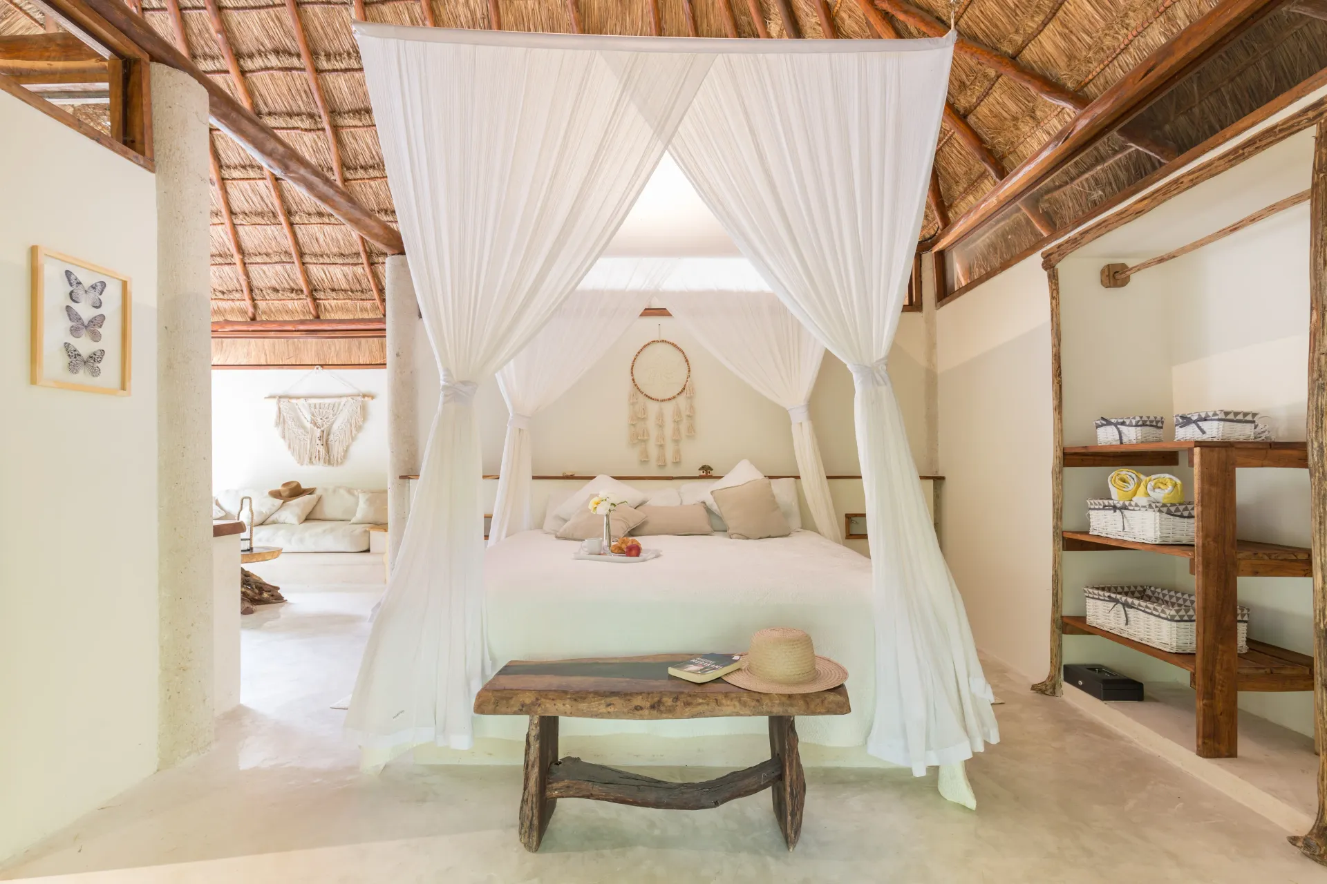 Dormitorio con cama con dosel, banco rústico y techo tejido en un entorno tropical.