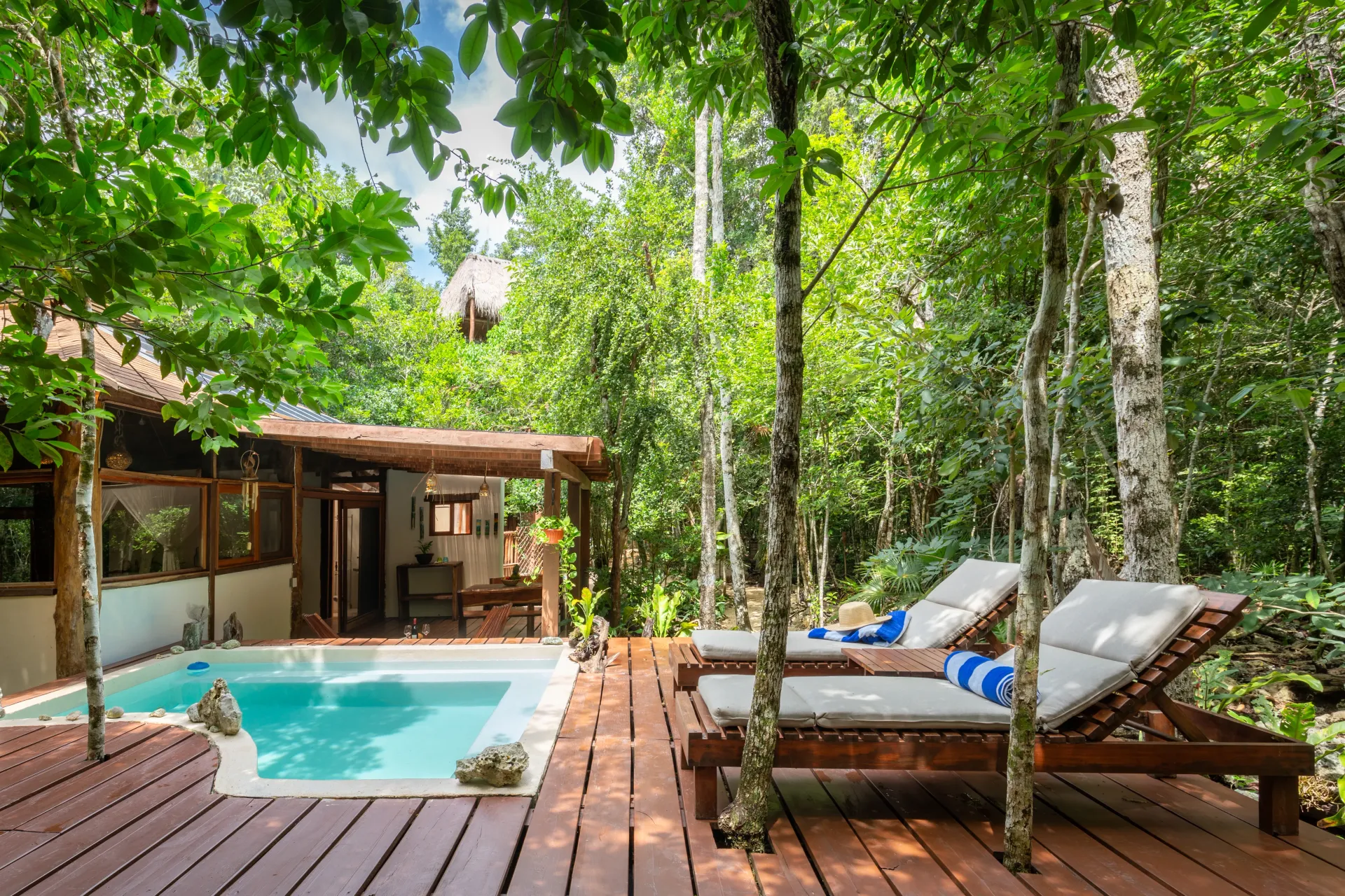 Villa junto a la piscina con tumbonas rodeadas de exuberantes árboles verdes.