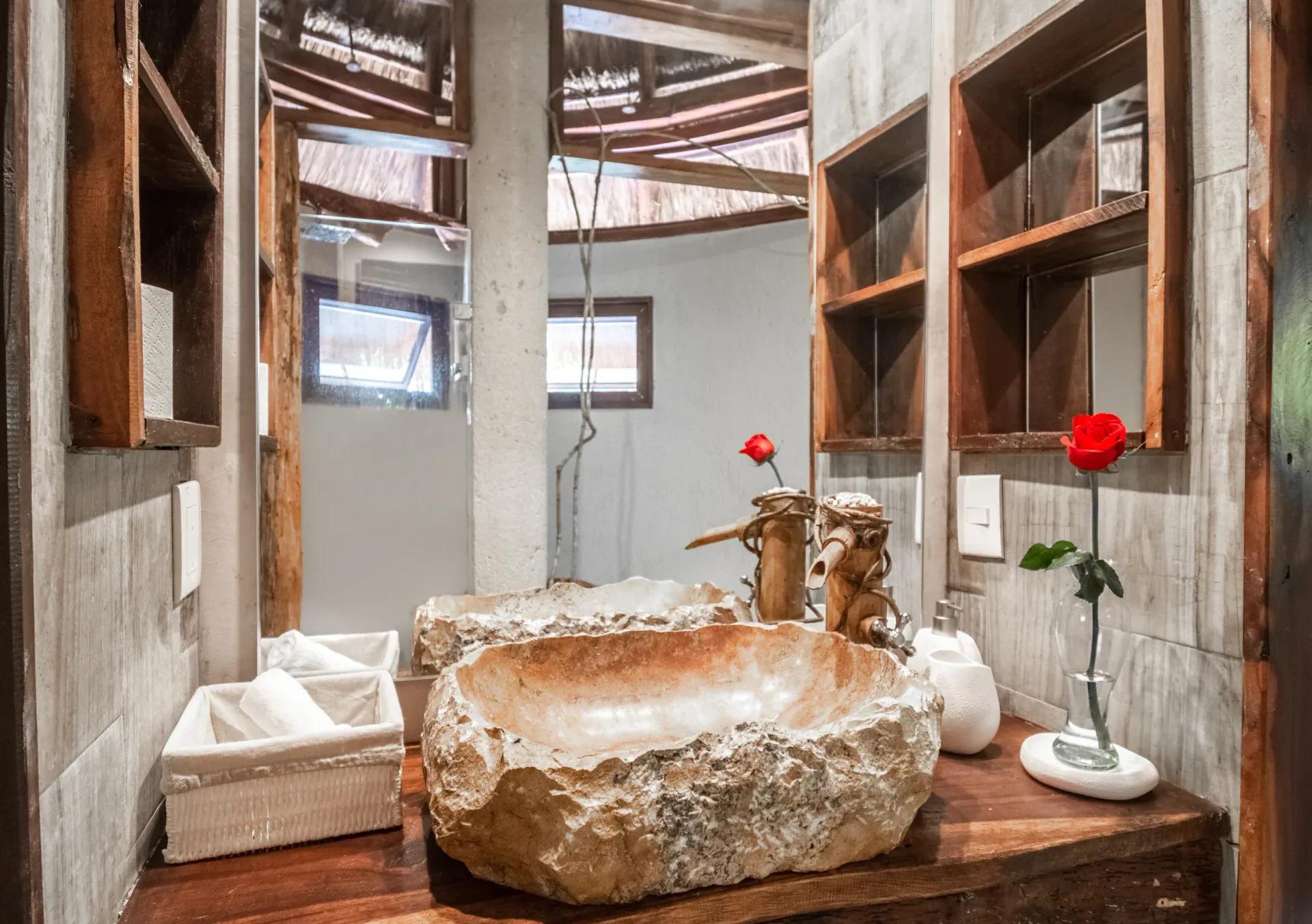 Baño rústico con lavabo de piedra, estantes de madera y una rosa roja.