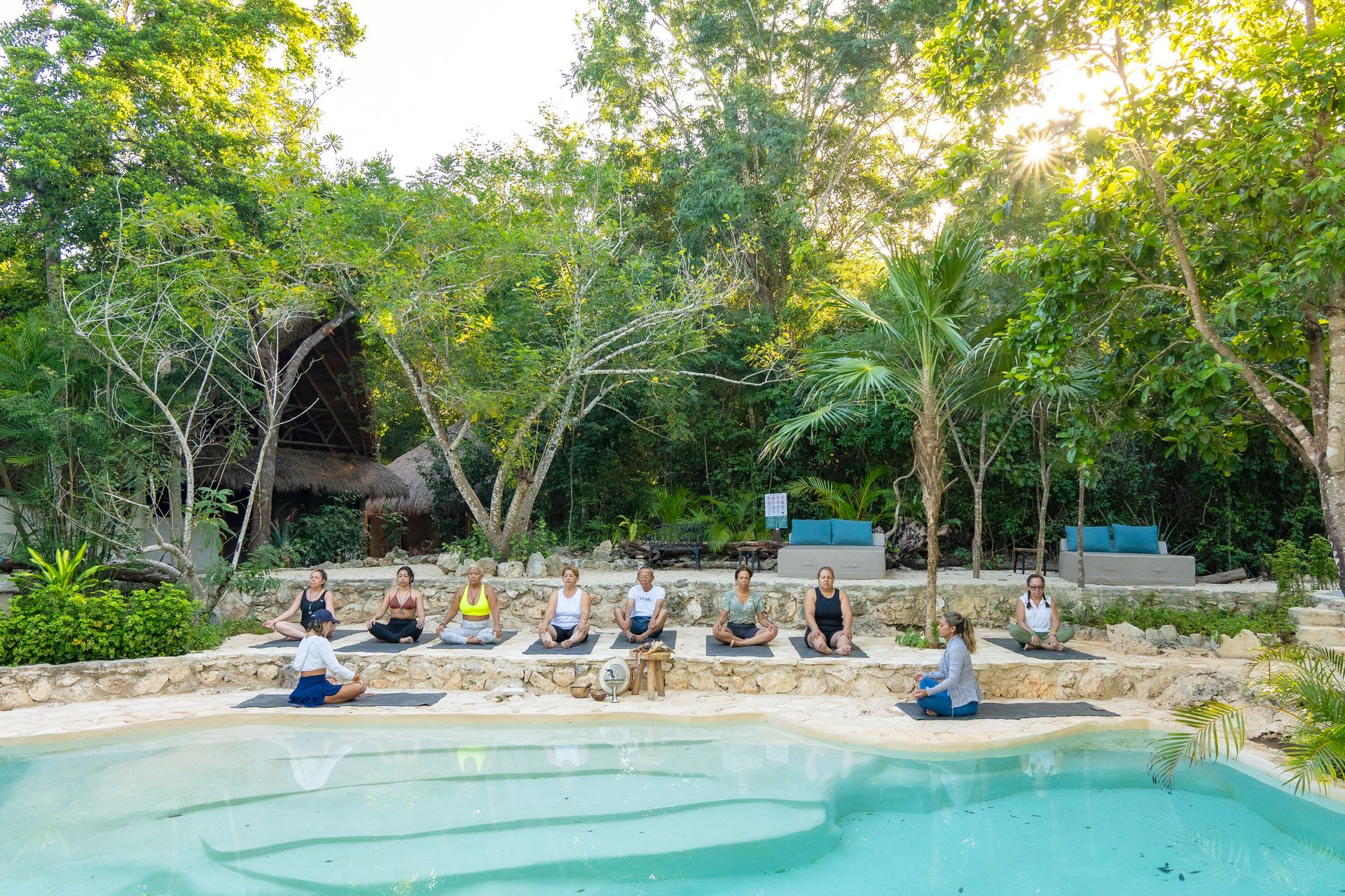 Grupo de personas meditando al borde de la alberca rodeada de naturaleza
