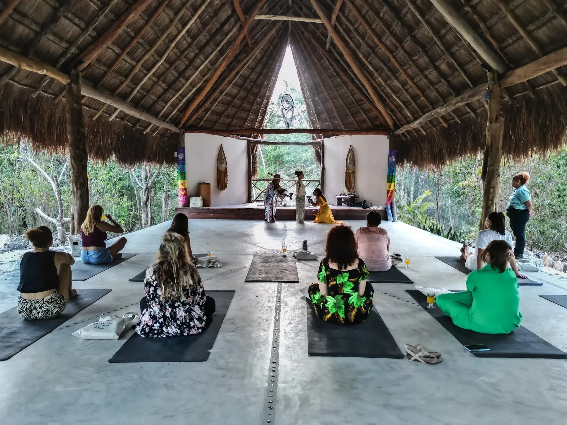 Personas en un estudio de yoga con techo de palapa. 