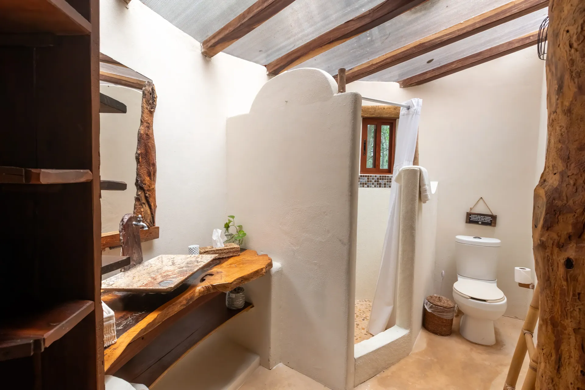 Baño rústico con tocador de madera, ducha abierta y WC.