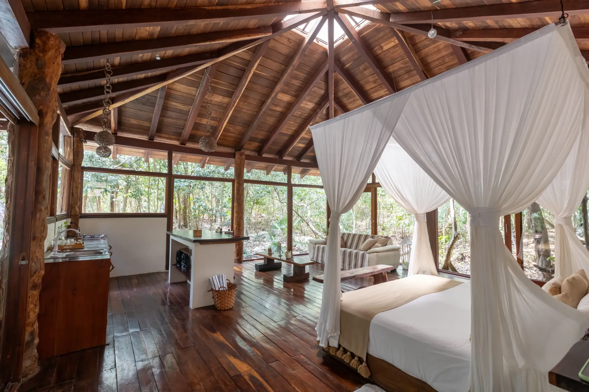 Dormitorio con cama con dosel y techo de madera, abierto a un frondoso y verde bosque.