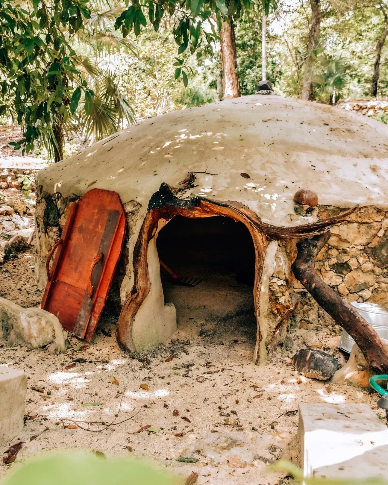 Horno de barro con techo abovedado y puerta abierta, situado en un claro de arena.