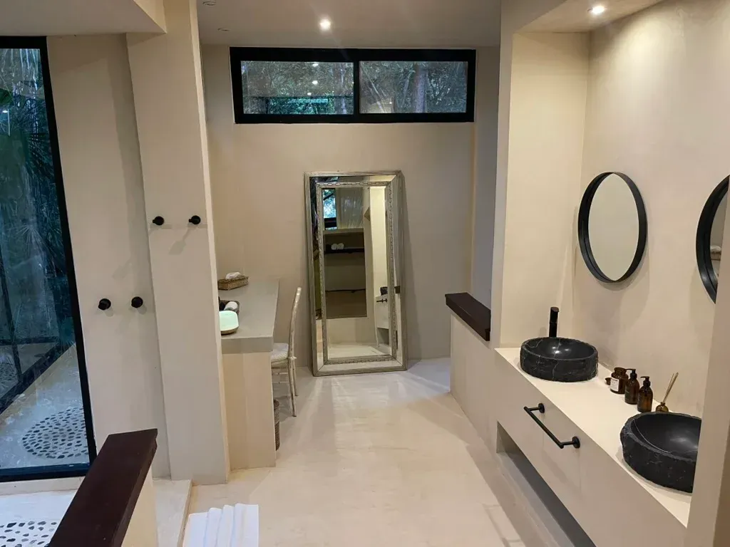 Baño moderno con dos lavabos negros, espejo grande y ventanas con marco negro.