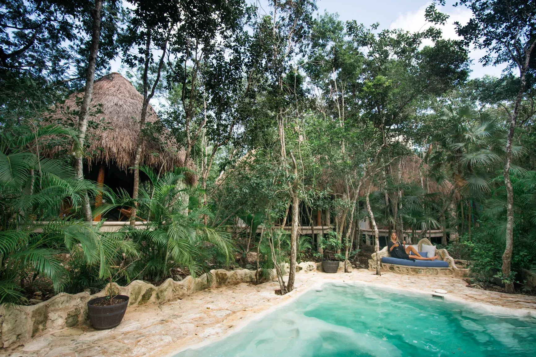 Retiro junto a la piscina en un entorno selvático con cabañas con techo de paja, exuberante vegetación .