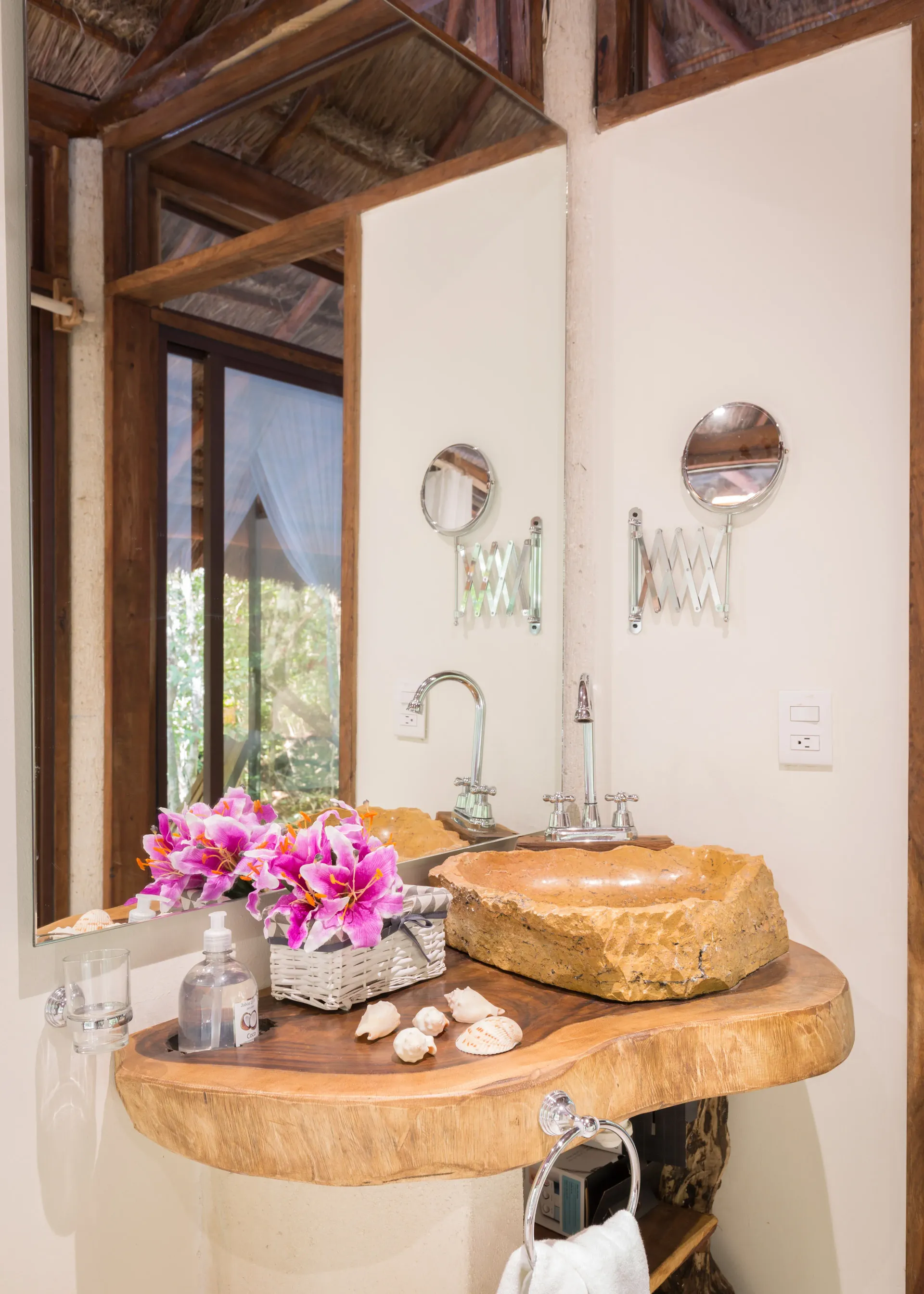 Mueble de baño con lavabo de piedra, arreglo floral y espejo. Detalles de madera en tonos neutros.