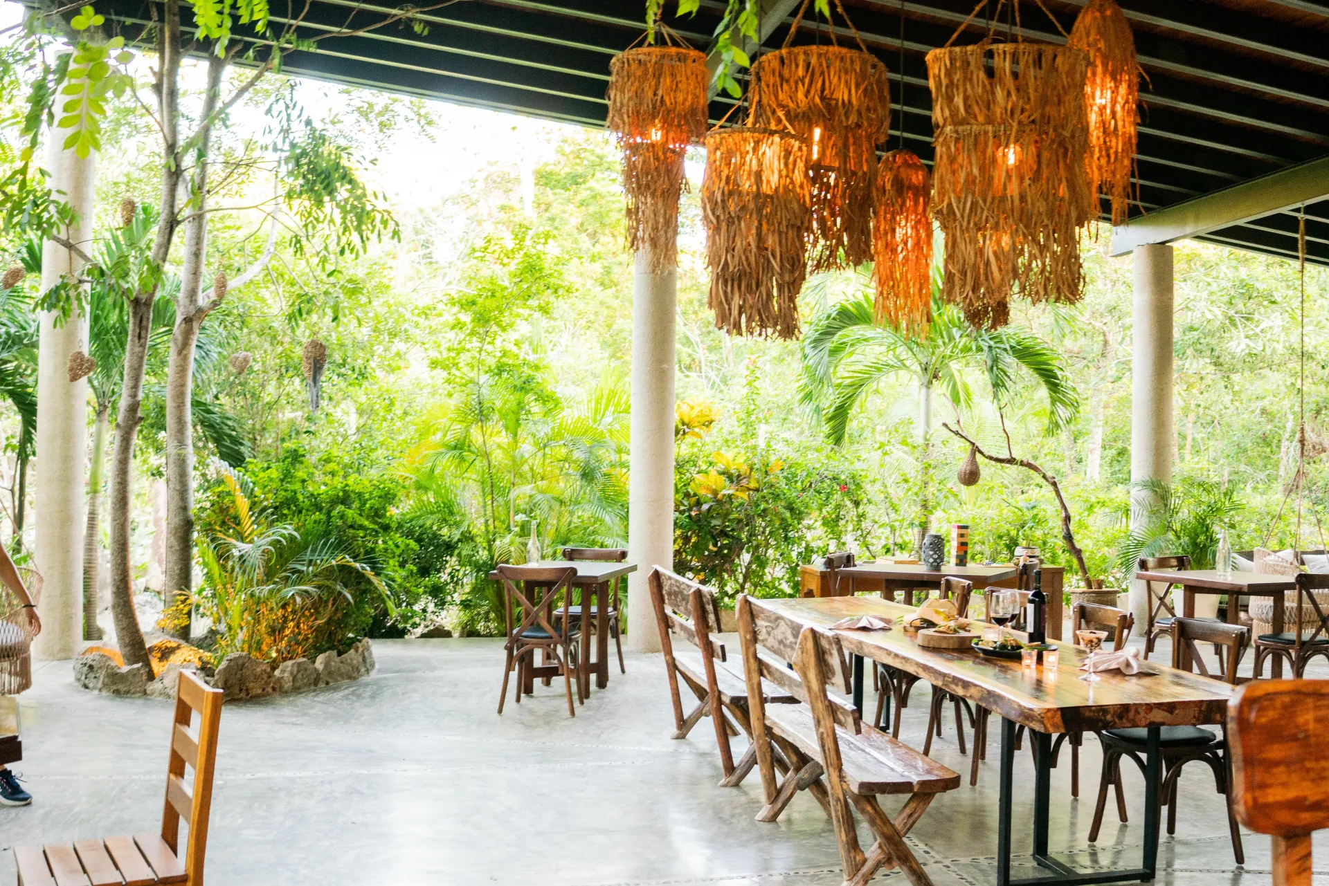 Restaurante al aire libre con mesas y sillas de madera, rodeado de exuberante vegetación.