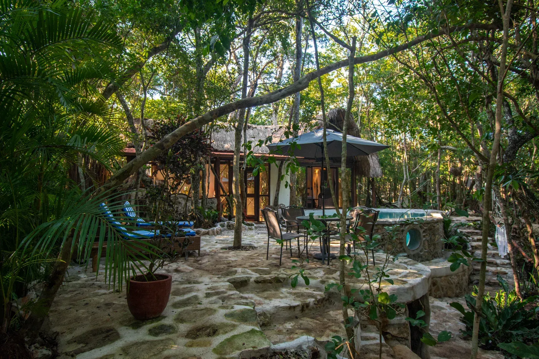 Un exuberante patio al aire libre con jacuzzi y zona de comedor rodeado de árboles.