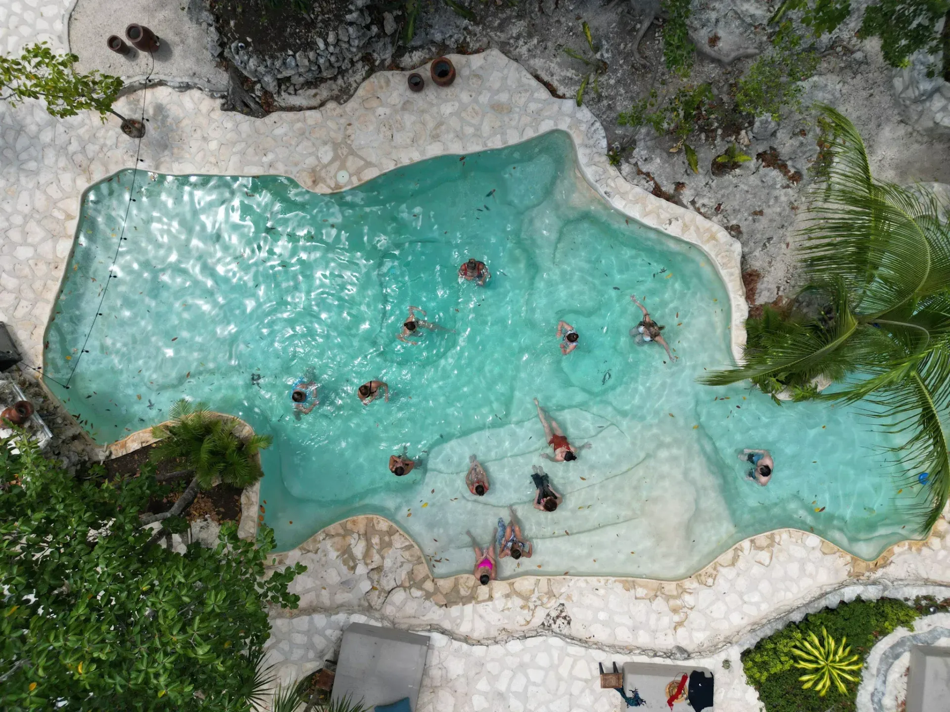 Vista aérea de la piscina turquesa llena de gente, rodeada de bordes rocosos y vegetación.