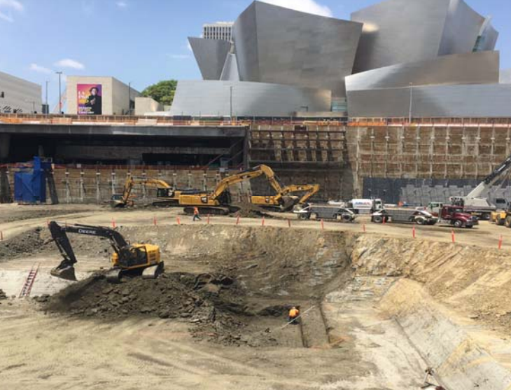Construction site with excavators and a deep excavation pit beside a large modern building
