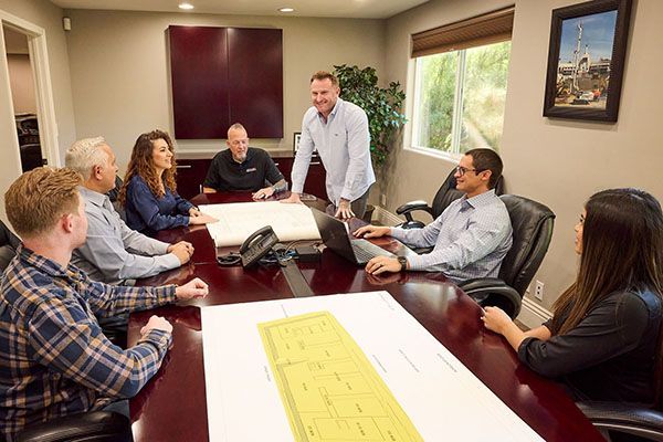 Meeting in a conference room around a table with laptops and papers, one person standing and speaking