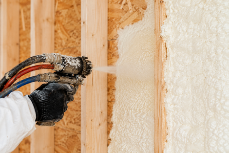 up close photo of a spray foam gun applying spray foam in between two wall studs