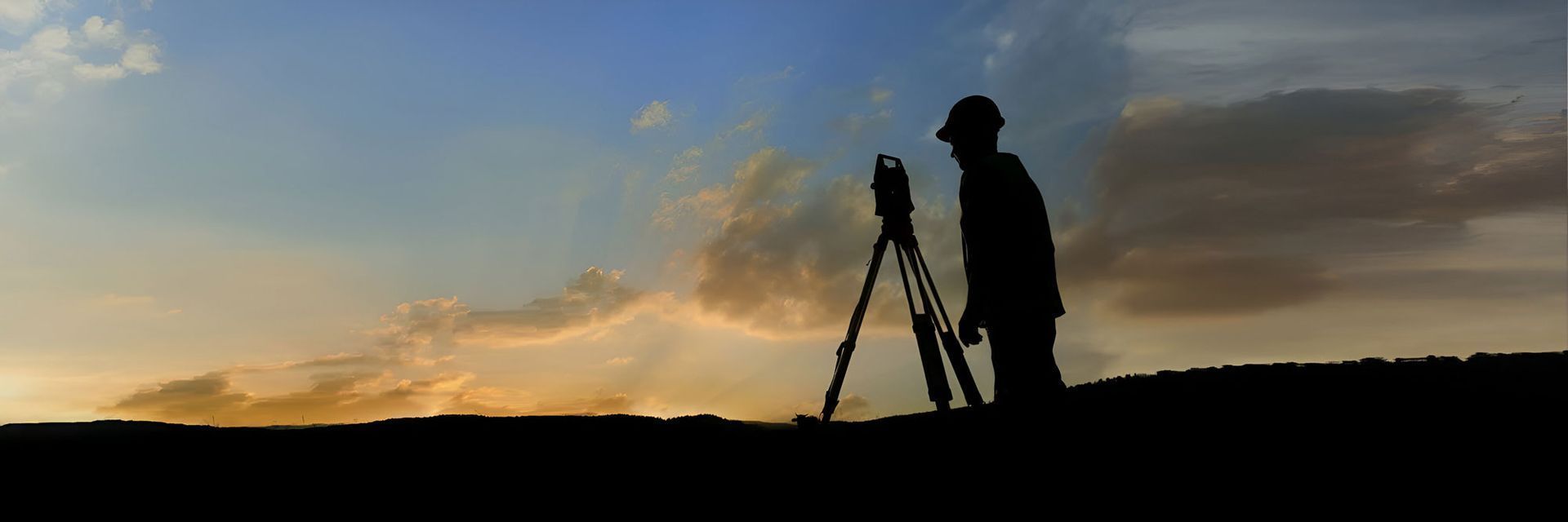 Una silueta de un hombre de pie junto a un trípode al atardecer.