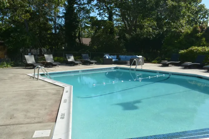 Outdoor swimming pool with blue water, lounge chairs, and trees in the background