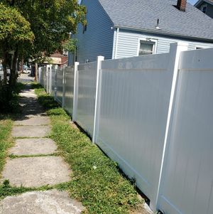 A white vinyl privacy fence runs alongside a concrete sidewalk next to a house on a sunny day.