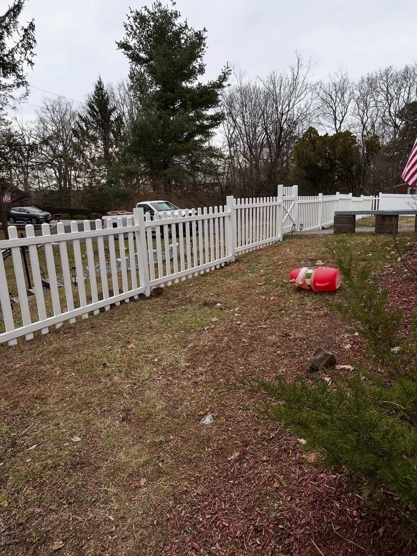 A white picket fence runs across a yard, with a small red toy lying on the grass in front of it under a cloudy sky.