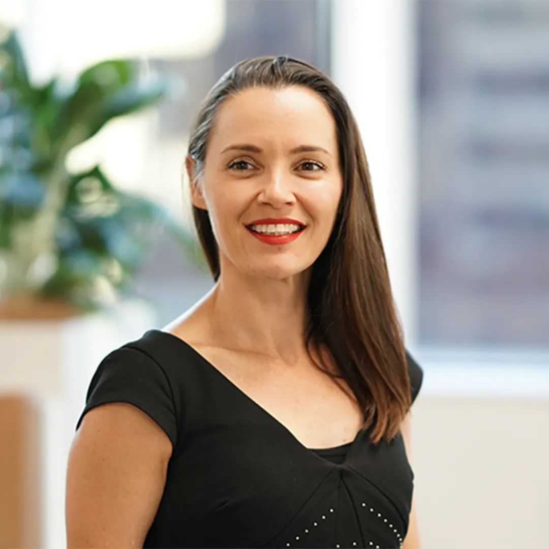 Woman with long brown hair, wearing a black top, smiling at the camera.