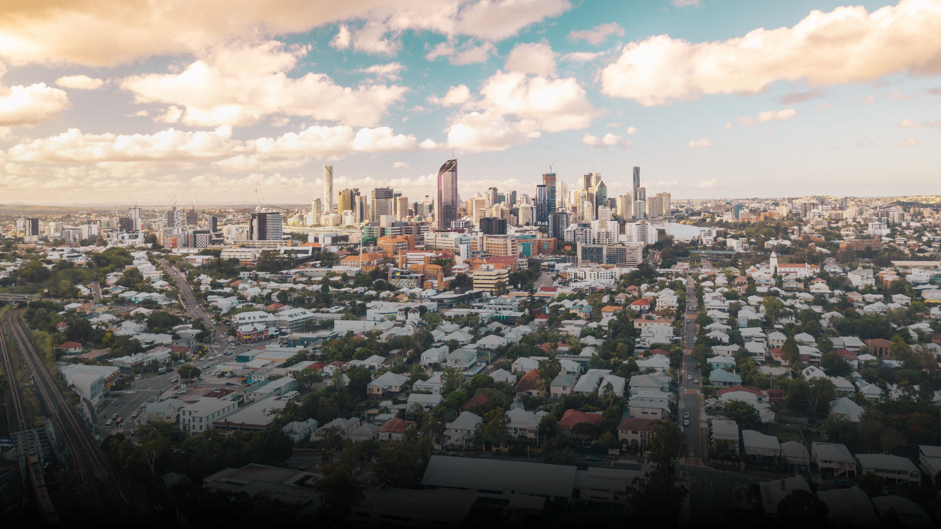 Cityscape with high-rise buildings, residential homes, and roads under a cloudy sky.