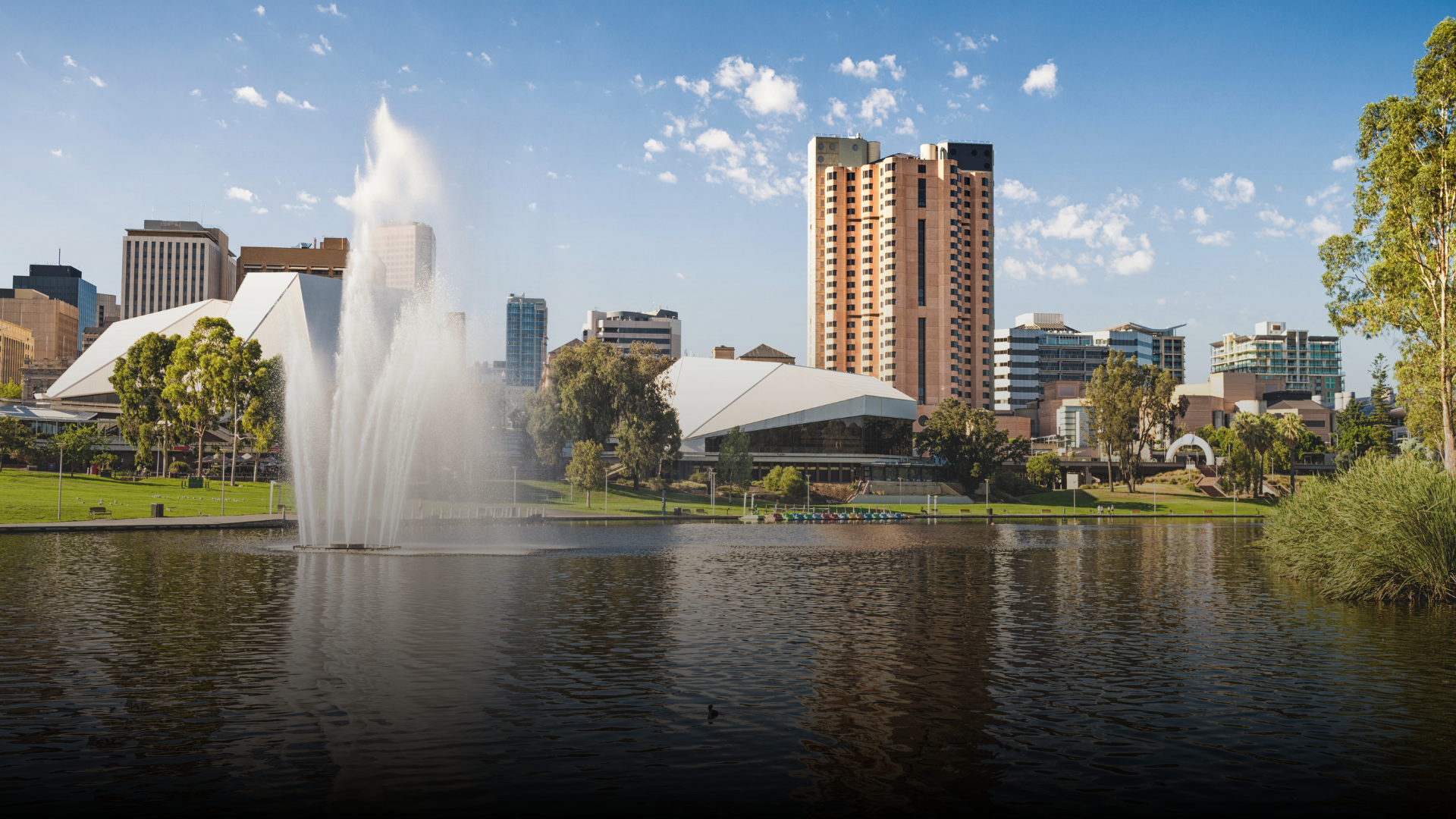 A city skyline with a tall fountain spraying water into a lake.