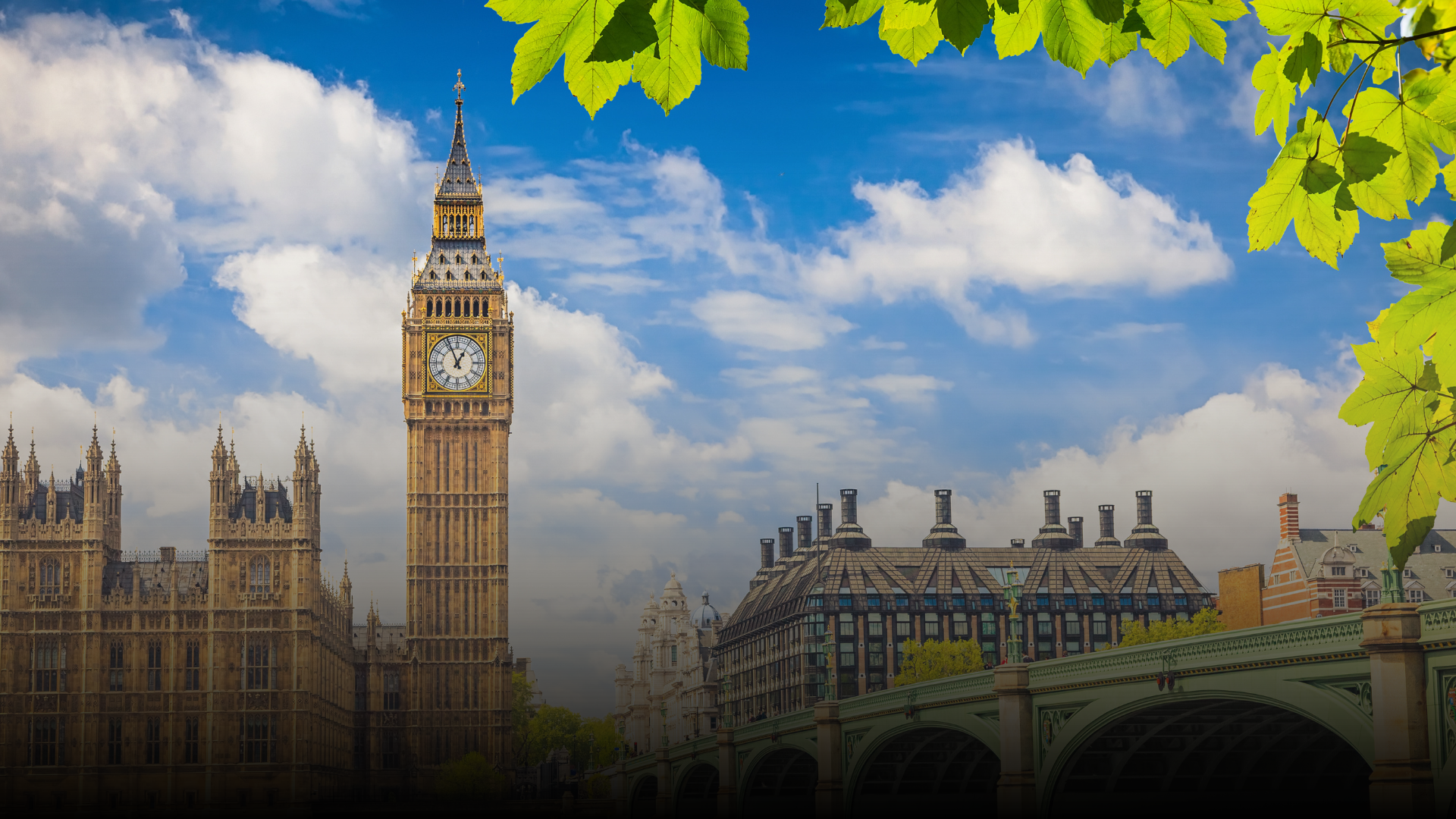 Big Ben clock tower and Houses of Parliament against a partly cloudy blue sky, with green foliage.