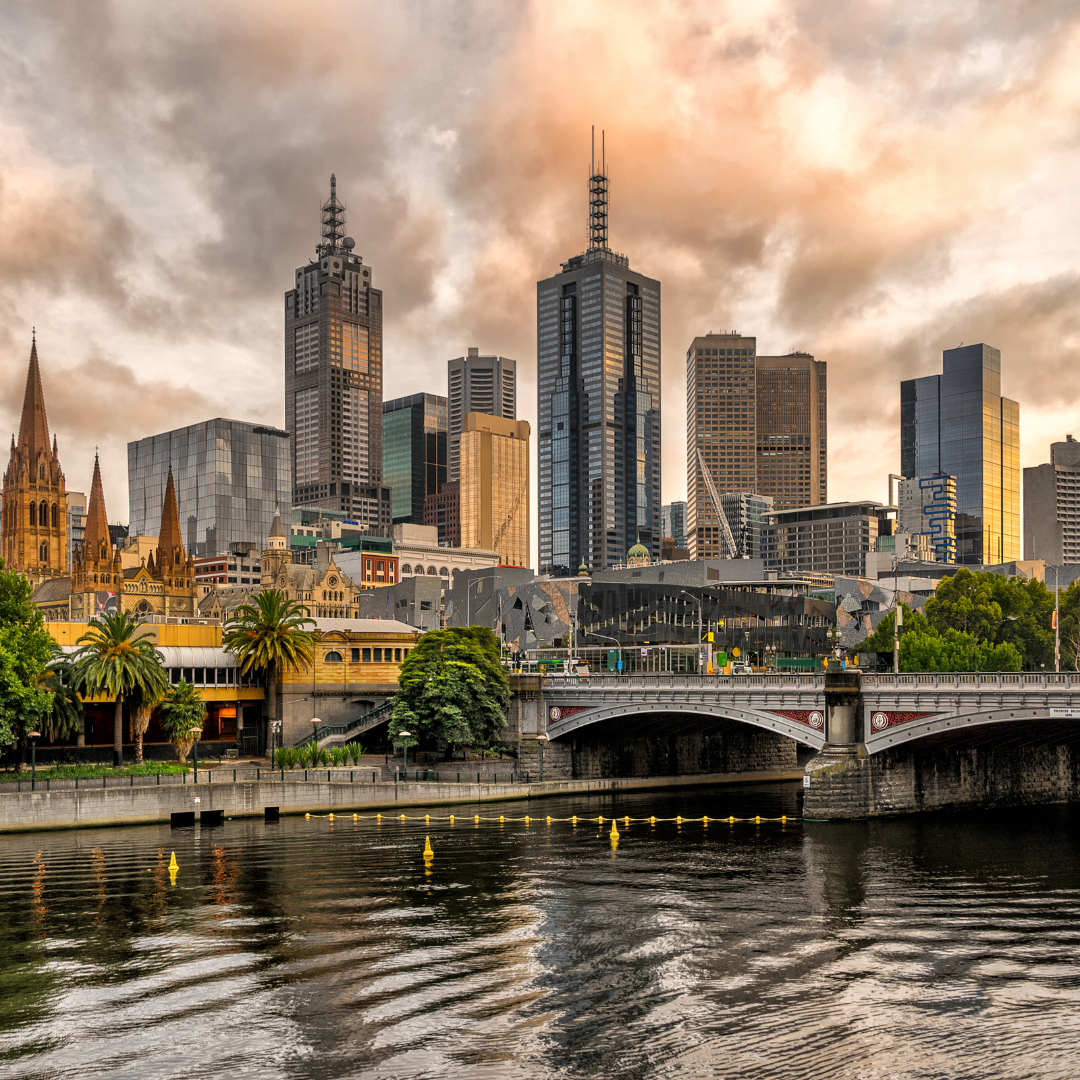 Skyline of Melbourne, Australia, with skyscrapers, bridge, and river. Cloudy sky.