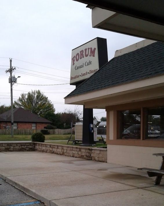 Exterior of a Forum Golf Club building with a sign, covered entrance, and sidewalk under cloudy skies