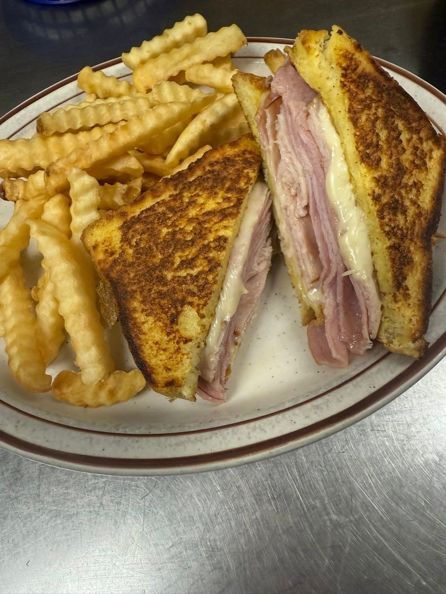 Grilled ham and cheese sandwich with crinkle-cut fries on a white plate