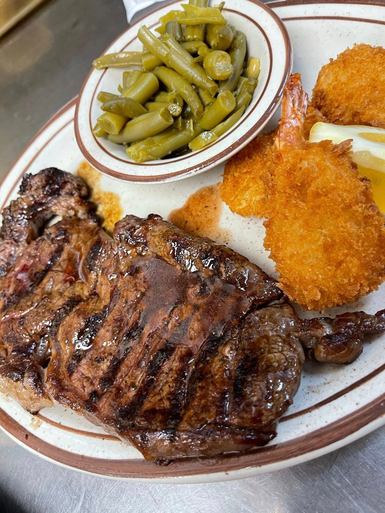 Plated steak with green beans and breaded shrimp, served with a side of green beans.
