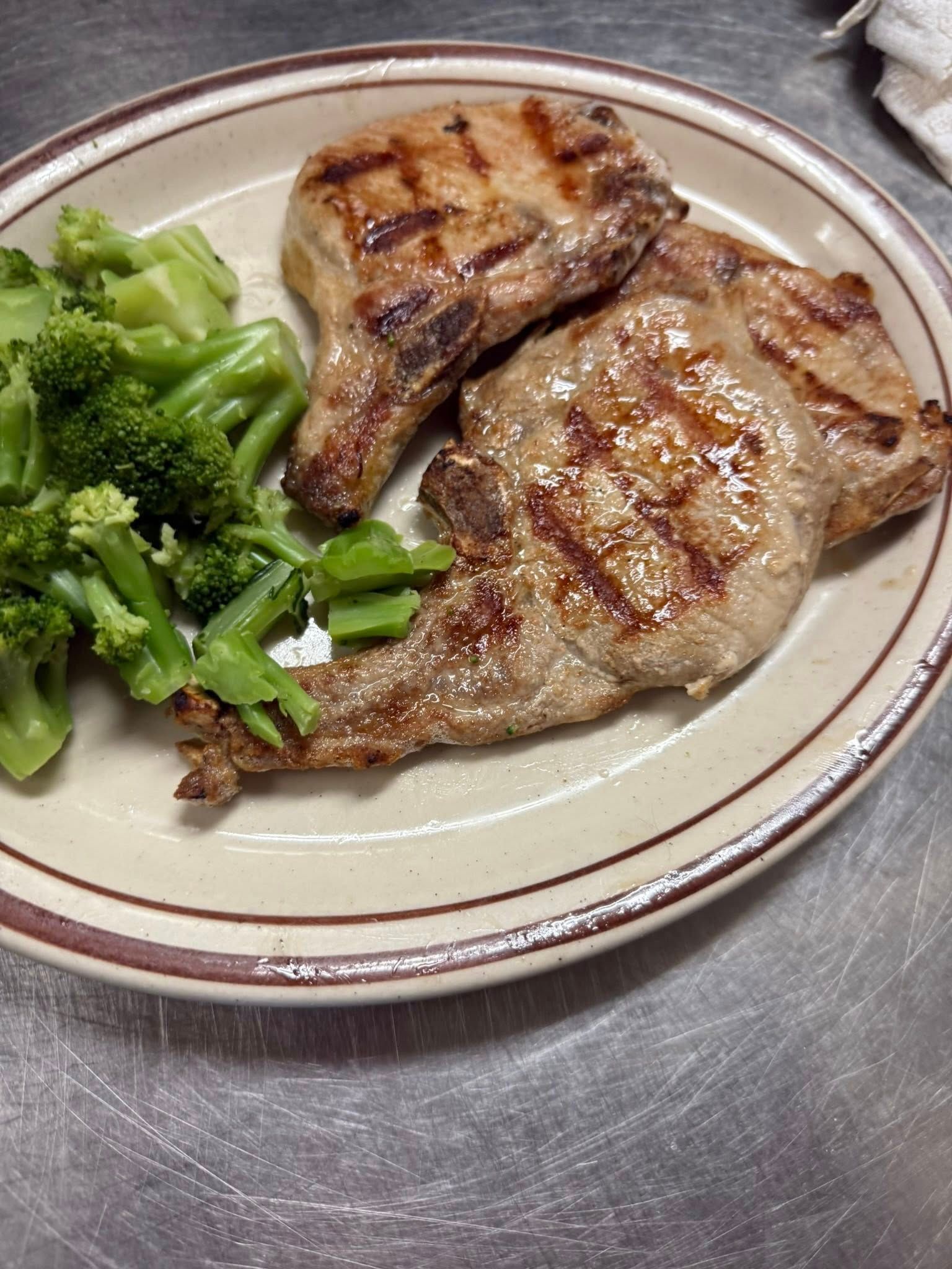 Two grilled pork chops on a plate with steamed broccoli and greens