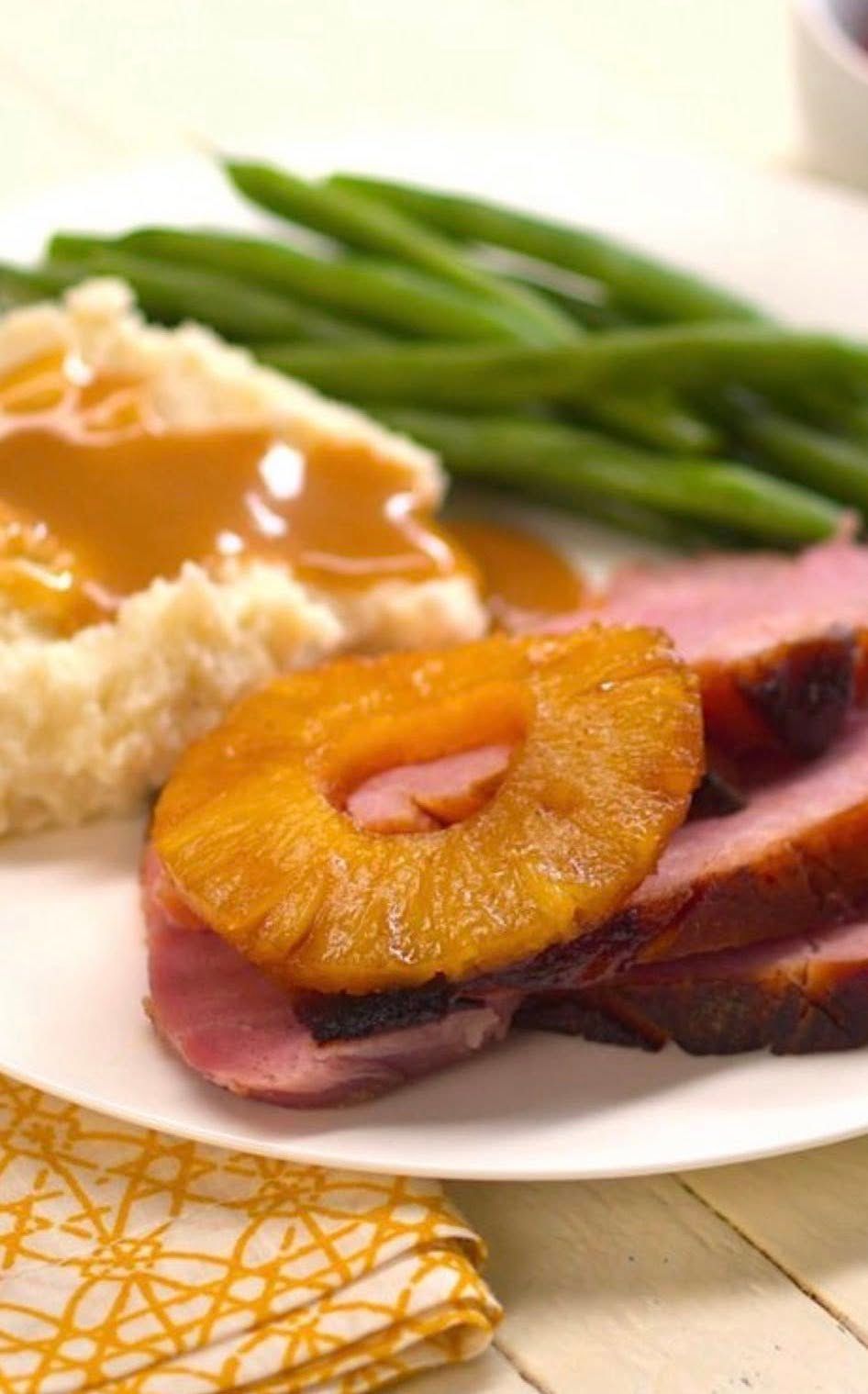 Plate with sliced meat, pineapple ring, green beans, and mashed potatoes on a table