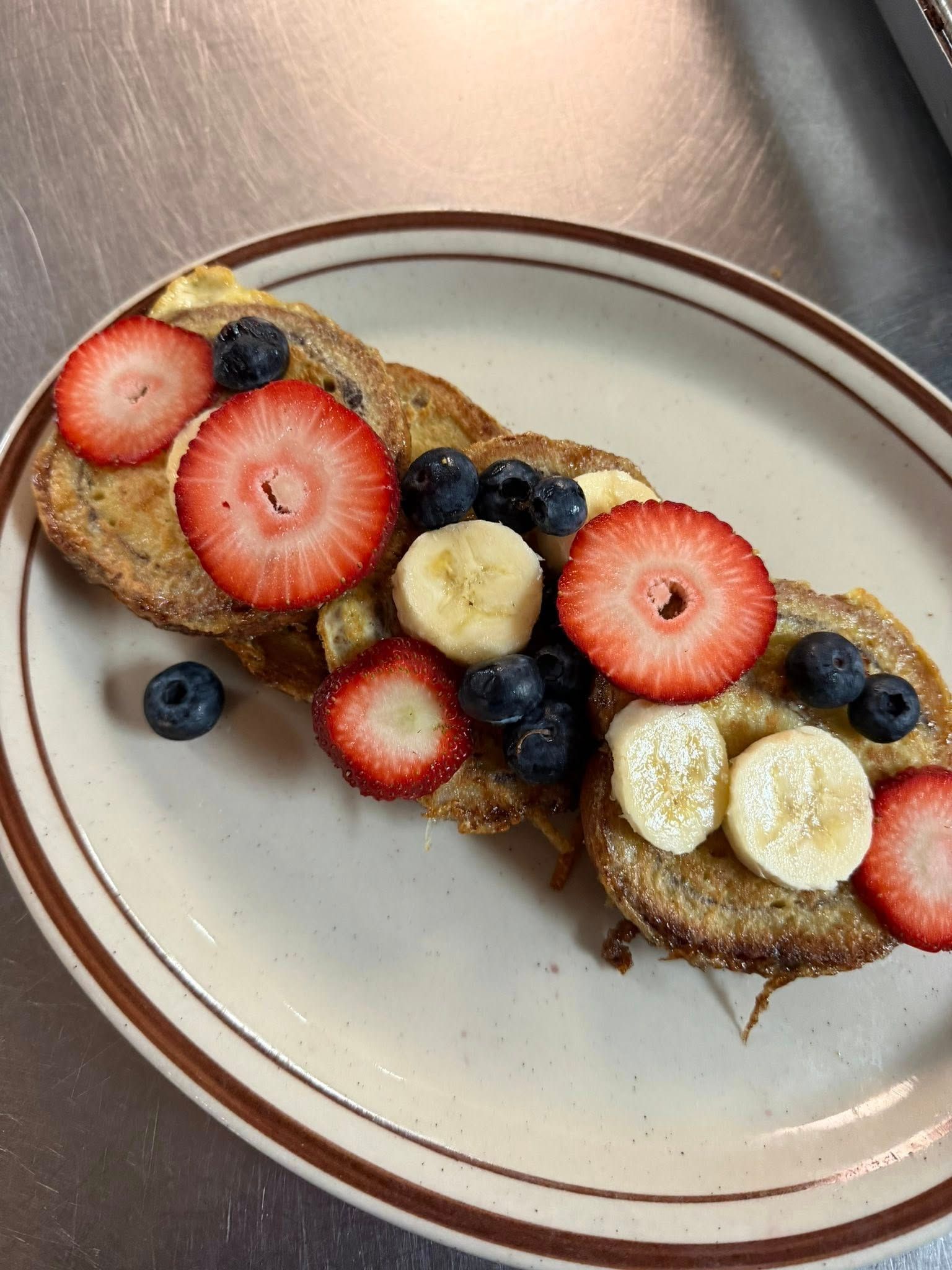 Two slices of toast topped with strawberry, banana, blueberries, and honey on a white plate