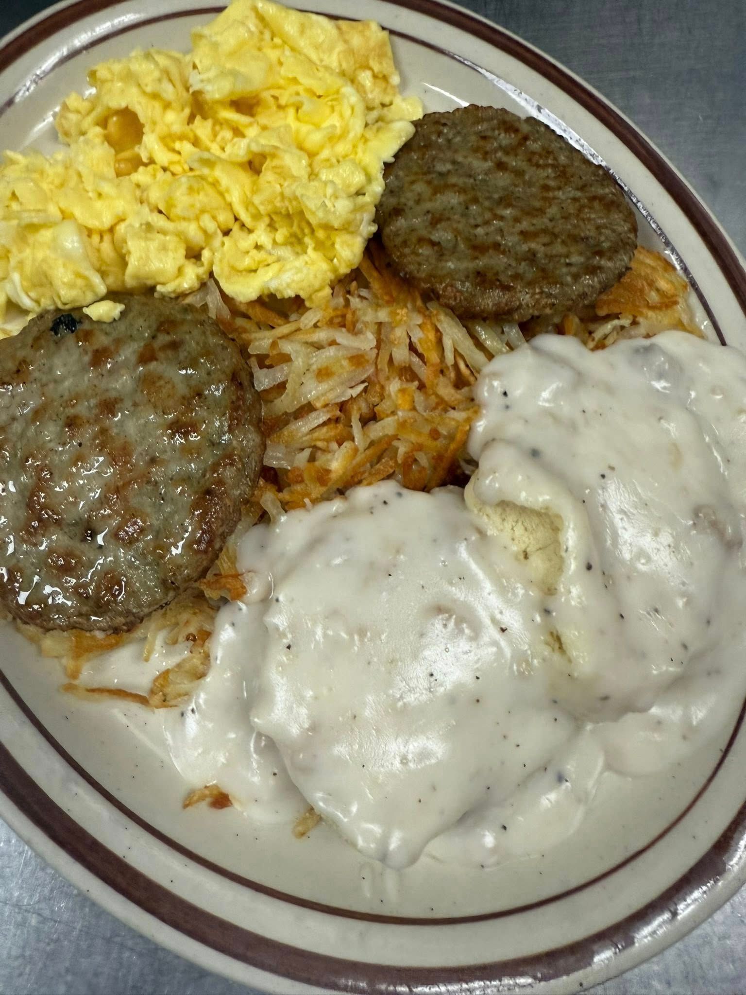 Plate of breakfast food with scrambled eggs, hash browns, sausage patties, and biscuits with white gravy
