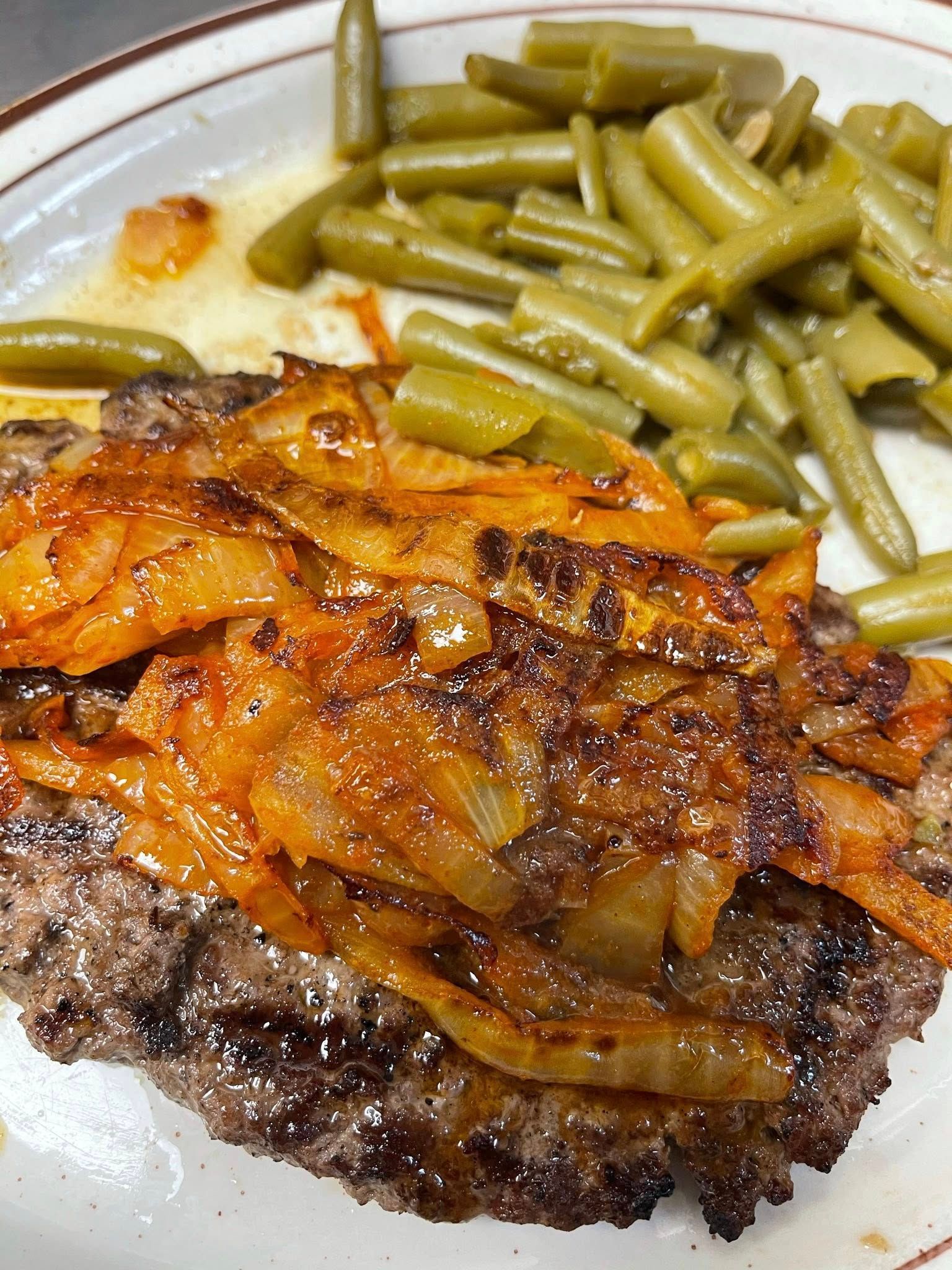 Plate with a grilled steak topped with caramelized onions and green beans on the side