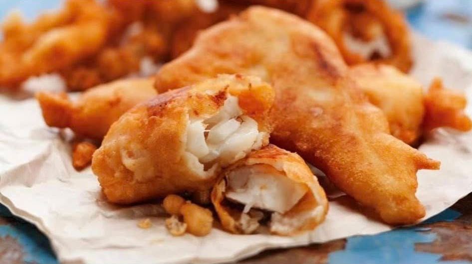 Fried fish fillets on a paper-lined tray, golden brown and crispy, with a close-up view of the flaky white interior