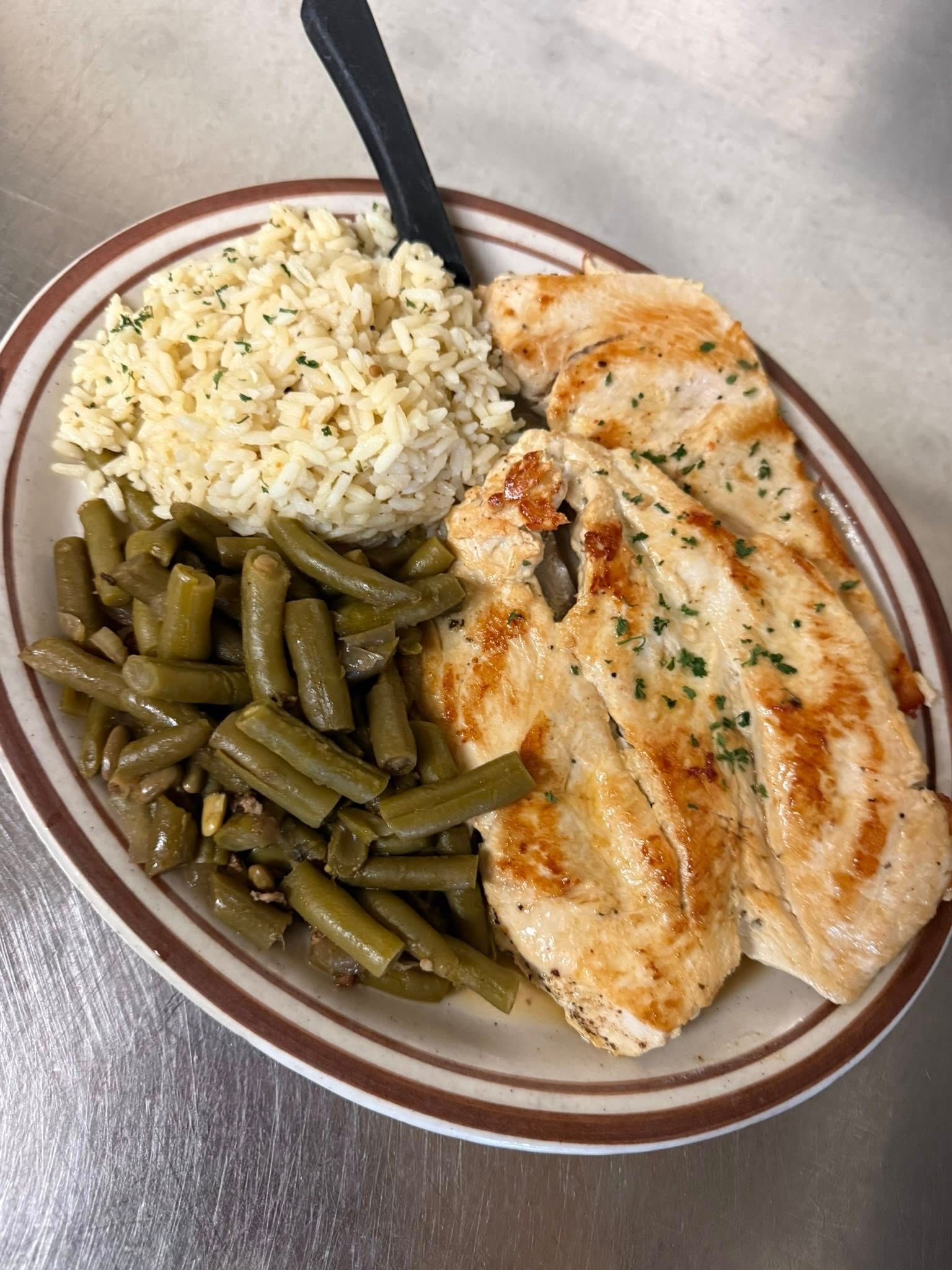 Plate with grilled chicken, rice, and green beans on a tabletop.