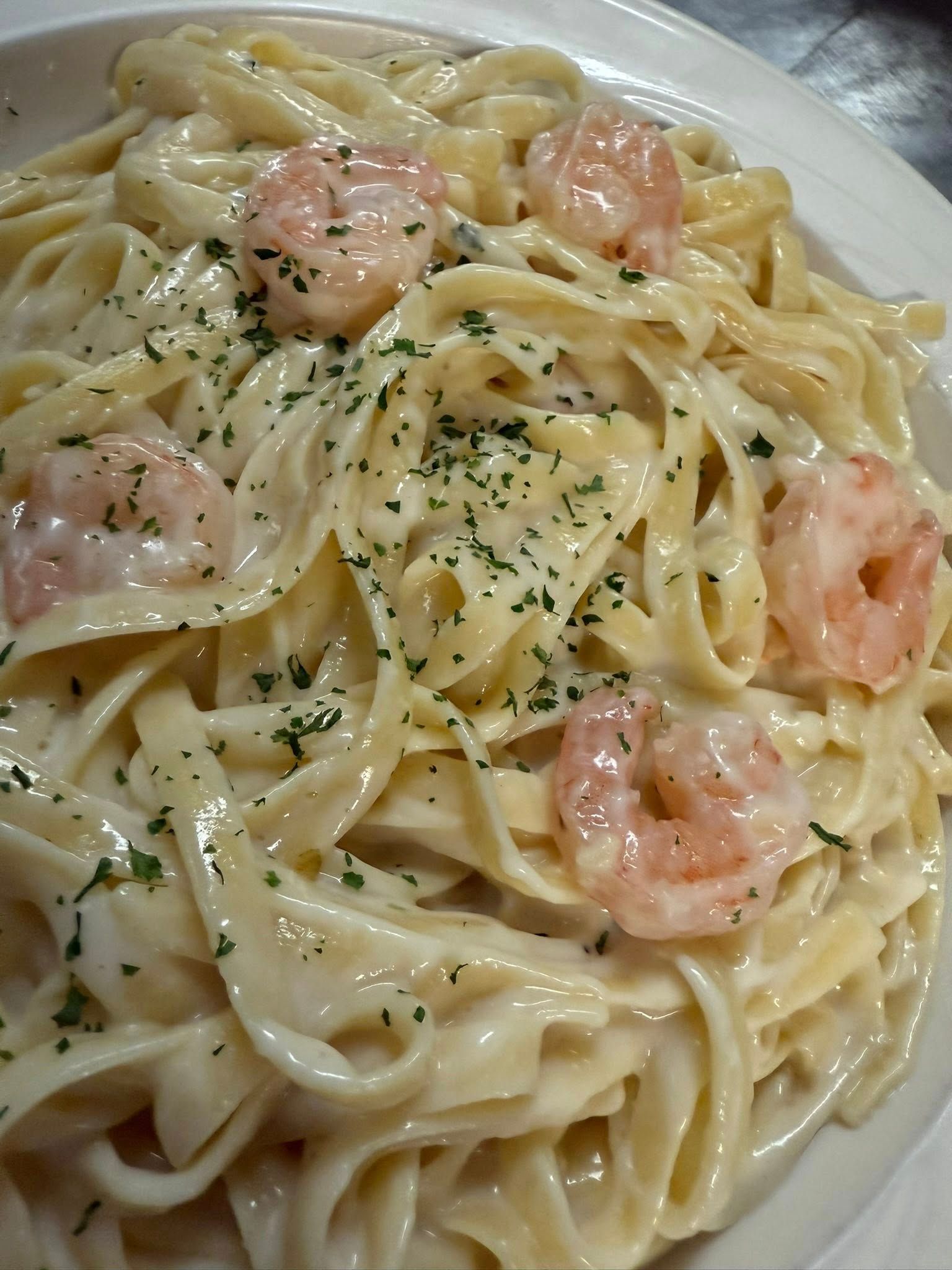 Creamy pasta with pink shrimp and parsley on a white plate