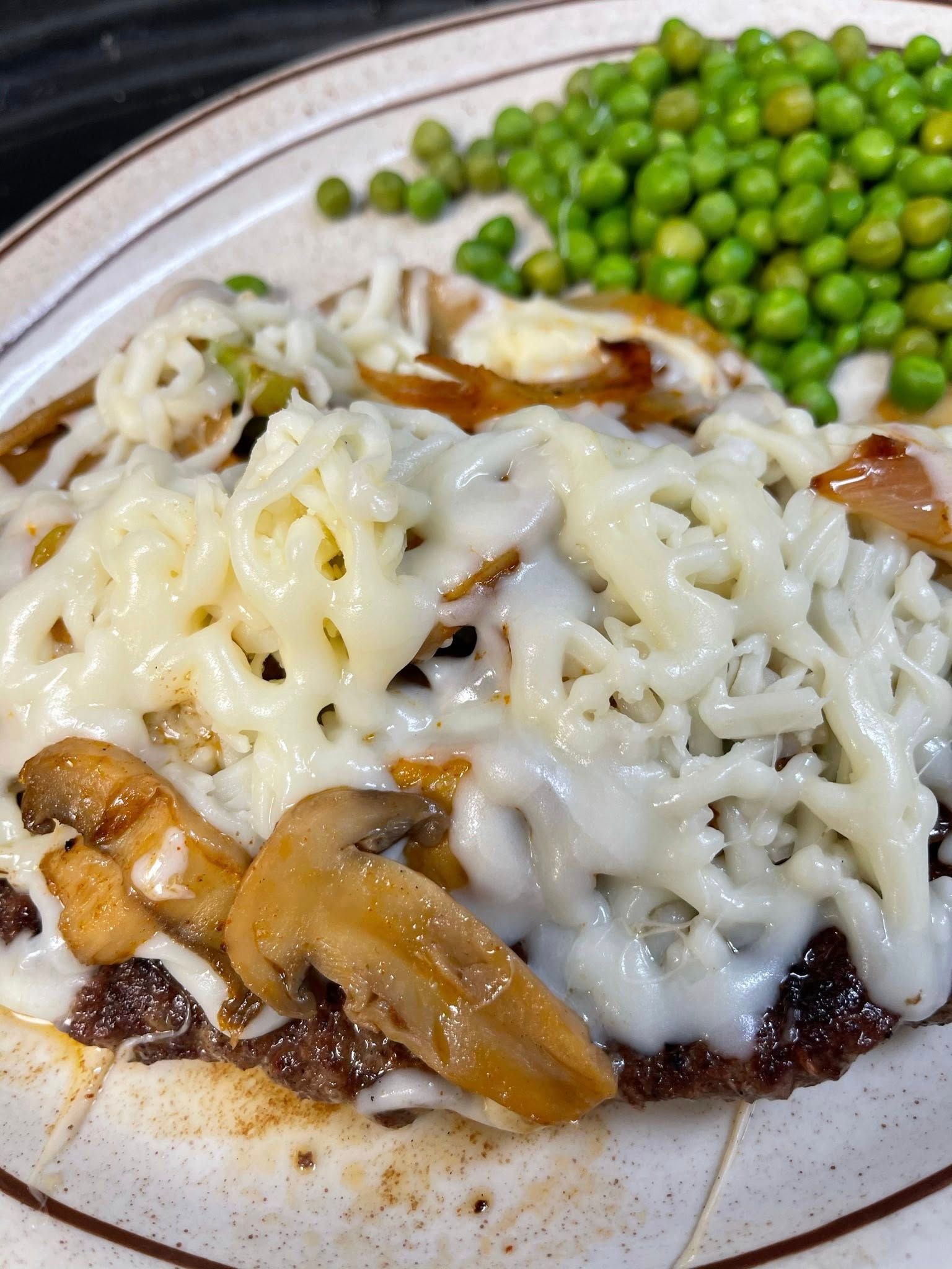 Melted cheese over chicken and mushrooms with peas on a dinner plate