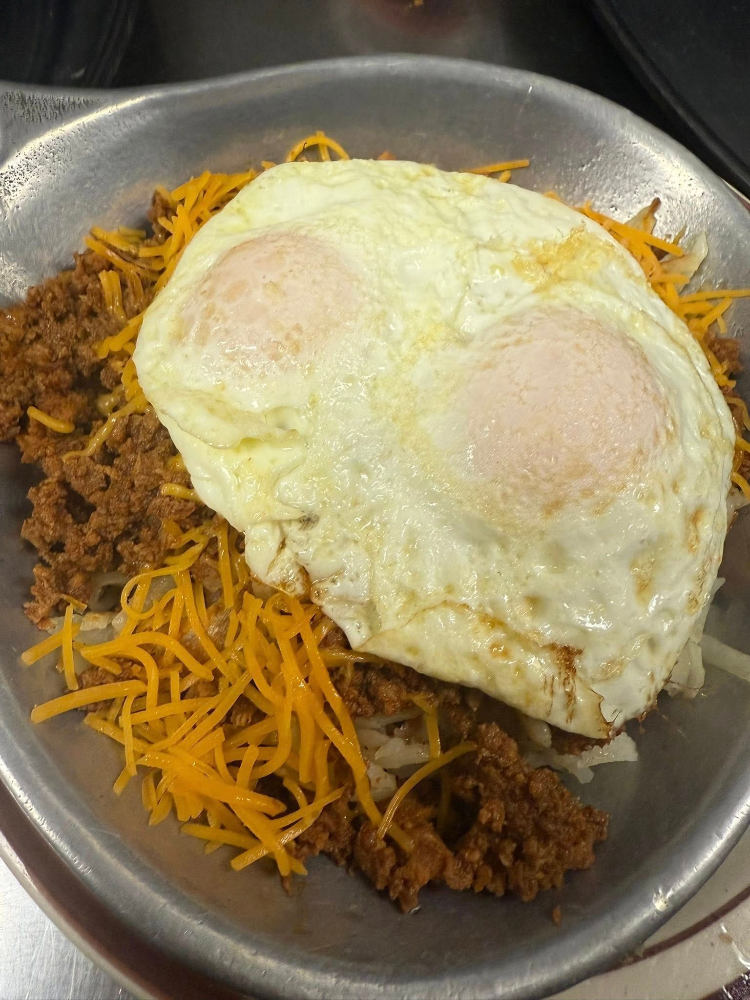 Fried eggs on shredded cheese and crumbled meat in a metal bowl