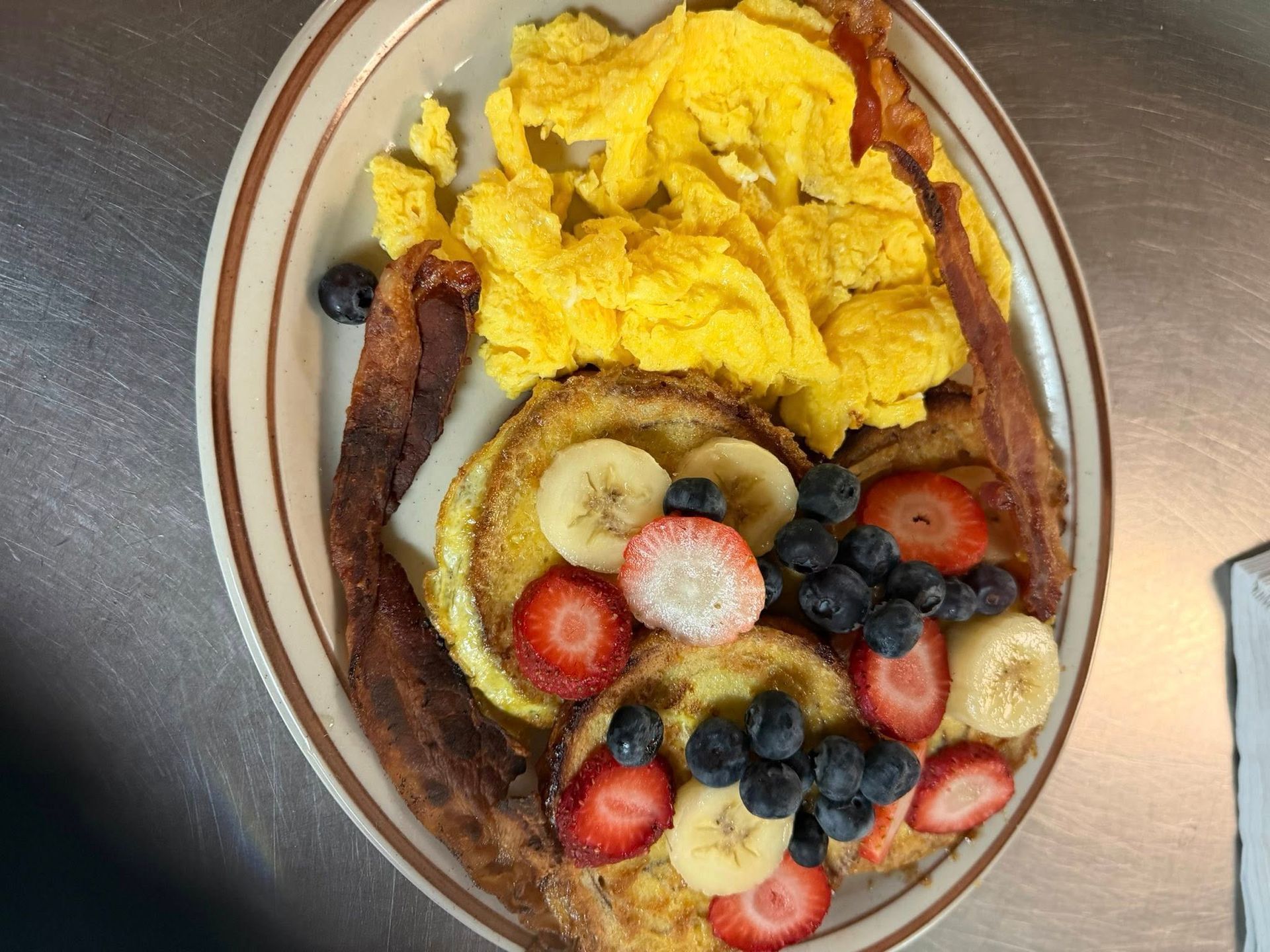 Breakfast plate with scrambled eggs and a berry-topped pancake or French toast with banana slices